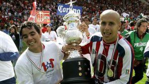 Adolfo “Bofo” Bautista y Omar Bravo celebran el campeonato del Apertura 2006 con las Chivas del Guadalajara, sosteniendo el trofeo que marcó una época dorada en el fútbol mexicano.
